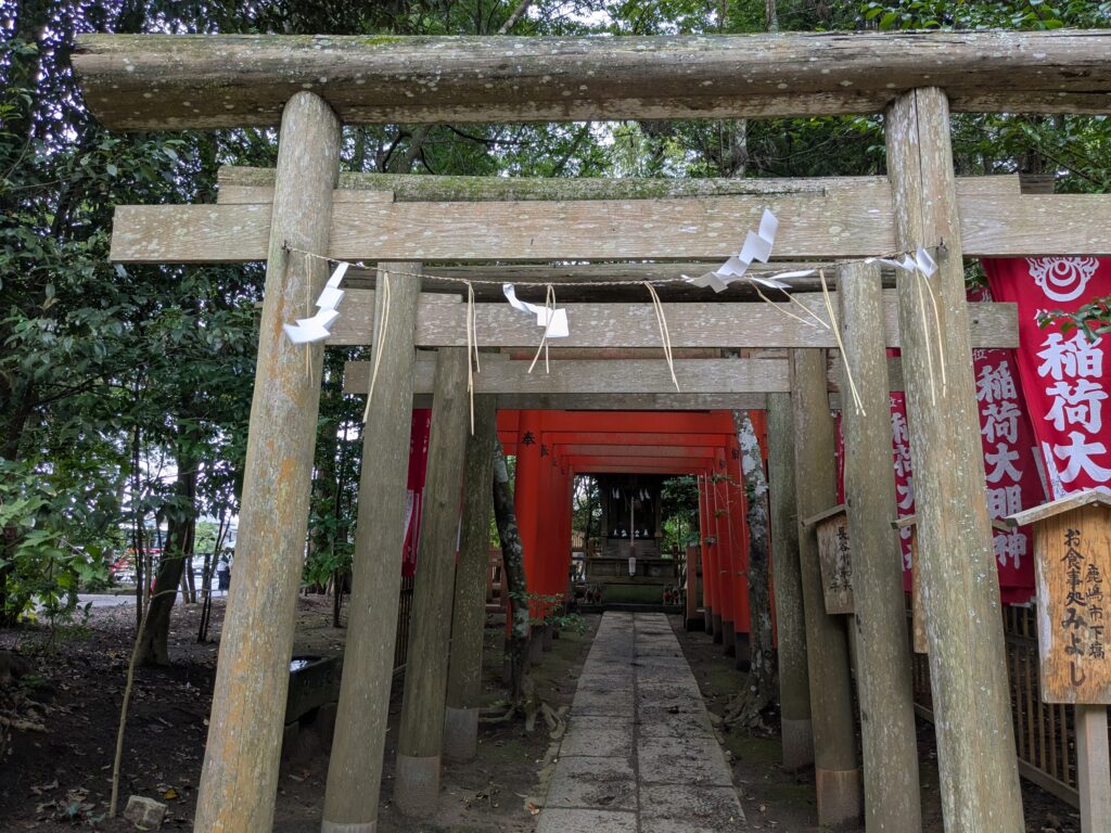 紙垂が掛けられた鳥居と朱色の鳥居が連なる稲荷社の参道